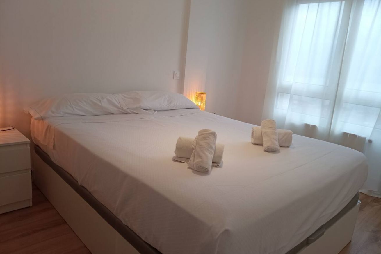 Ein ordentlich bezogenes Bett mit weißen Leinen und Handtüchern, ein Nachttisch und ein Fenster mit Vorhängen.