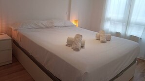 A neatly made bed with white linens and towels, a bedside table, and a window with curtains. - C01A01 Apartamento Moderno con vistas al mar (Santander)
