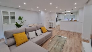 Una sala de estar moderna con un sofá, una mesa de centro de vidrio y una cocina al fondo.