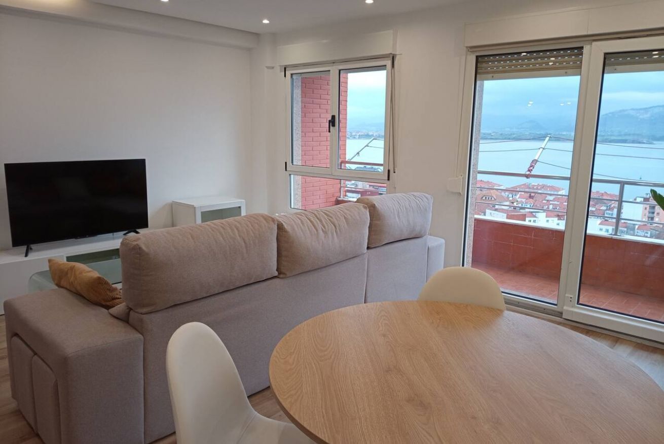Una sala de estar moderna con un sofá, un televisor y un balcón con vistas a un puente y edificios.