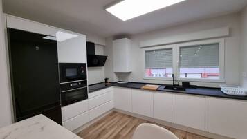 A modern kitchen with white cabinets, a black microwave, and a window with blinds.