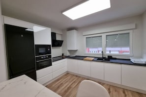 A modern kitchen with white cabinets, a black microwave, and a window with blinds. - C01A01 Apartamento Moderno con vistas al mar (Santander)