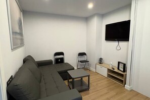 Una sala moderna con un sofá seccional, una mesita, dos sillas, un televisor montado en la pared y piso de madera.