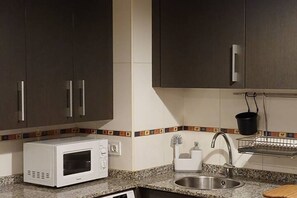 Een keuken met donkere kastjes, een magnetron, een spoelbak en een betegelde achterwand.