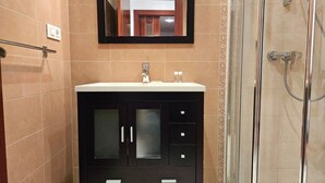 Ein Badezimmer mit Waschtisch, Spiegel, Dusche und gefliesten Wänden.