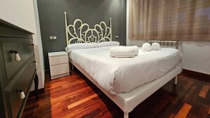 Ein modernes Schlafzimmer mit Bett, Nachttisch, Kommode und einem Fenster mit Vorhängen.