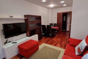 Un salon équipé d’un téléviseur à écran plat, d’un canapé rouge, d’un meuble en bois et d’un coin repas avec une table et des chaises rouges.