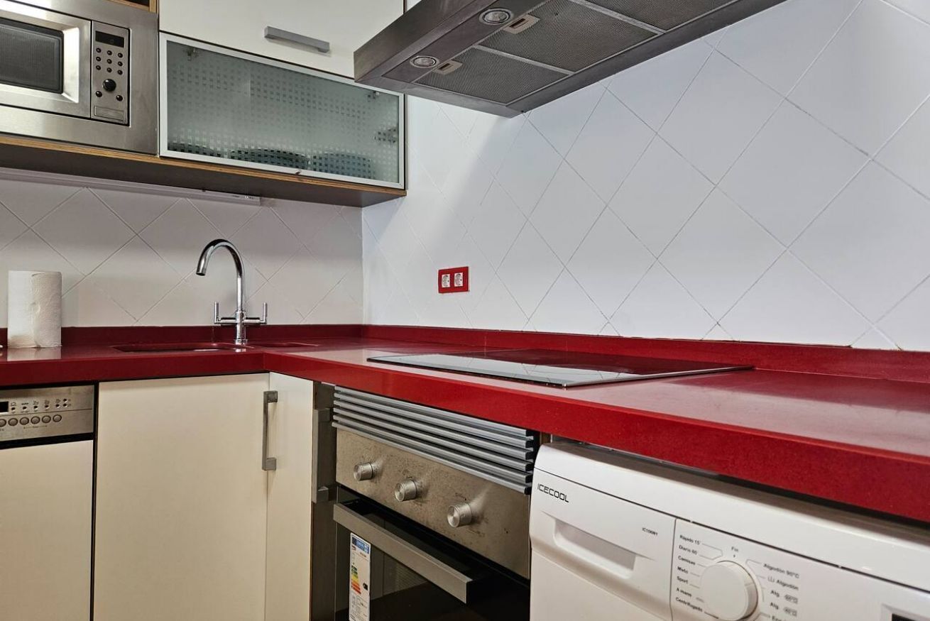 A kitchen with a red countertop, stainless steel appliances, and a white tiled backsplash.