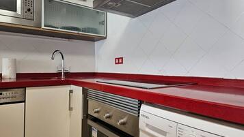 A kitchen with a red countertop, stainless steel appliances, and a white tiled backsplash.