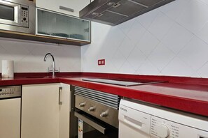 Une cuisine dotée d’un plan de travail rouge, d’appareils électroménagers en acier inoxydable et d’un dosseret de carrelage blanc.