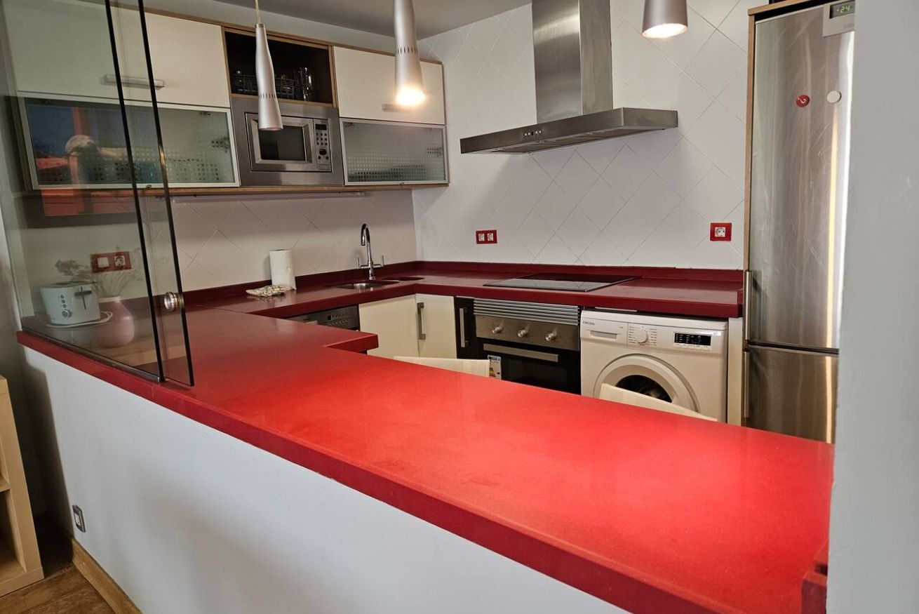 Una cocina con encimera roja, electrodomésticos de acero inoxidable, microondas, estufa y lavadora.