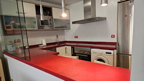 A kitchen with a red countertop, stainless steel appliances, a microwave, a stove, and a washing machine. - 130A Beautiful Apartment in Cimadevilla by R2R (Gijón)