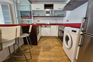 Une cuisine compacte équipée d’un four à micro-ondes, d’un lave-linge et d’un petit coin bar avec des tabourets.