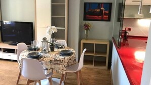A dining area with a table set for four, a television, a vase with flowers, and a painting on the wall. - 130A Beautiful Apartment in Cimadevilla by R2R (Gijón)