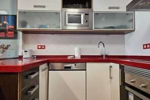 Cuina compacta amb microones, rentaplats i un taulell vermell.