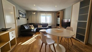 A modern living room with a black leather sofa, a round dining table with chairs, a TV, and a large cabinet. - 130A Beautiful Apartment in Cimadevilla by R2R (Gijón)