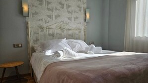 A neatly made bed with white linens and a brown blanket, a small wooden stool, and a wall-mounted light fixture. - 130A Beautiful Apartment in Cimadevilla by R2R (Gijón)