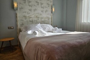 A neatly made bed with white linens and a brown blanket, a small wooden stool, and a wall-mounted light fixture. - 130A Beautiful Apartment in Cimadevilla by R2R (Gijón)