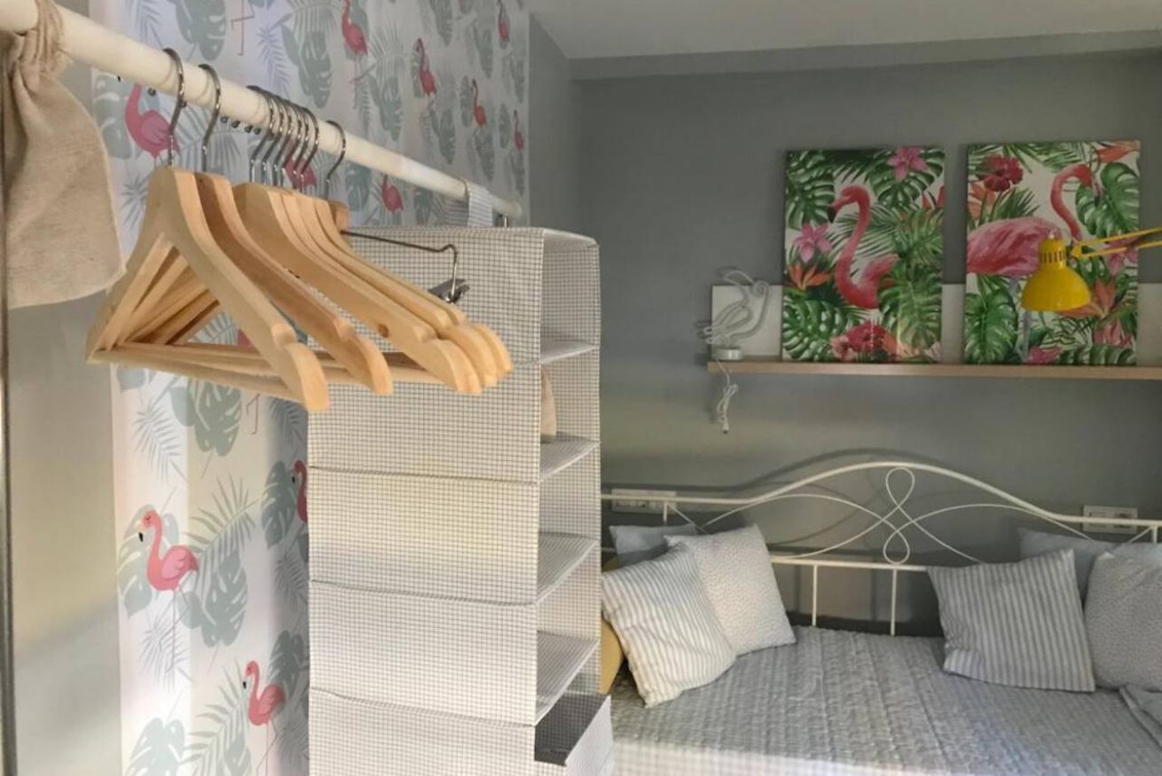 Une chambre à coucher avec un lit, un portant à vêtements, une étagère avec des tableaux et un rideau orné d’un motif de flamants roses.