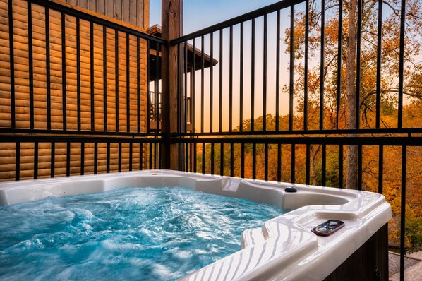 A hot tub with a wooden deck and metal railing, surrounded by trees with autumn foliage.