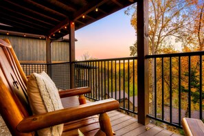 A wooden deck with a railing, a bench, and a view of trees and a house in the background. - PForge Cabin | Indoor Pool, Theater, Game Room (Pigeon Forge)