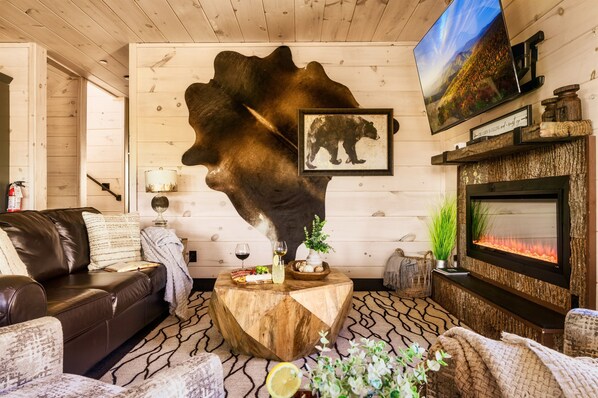 A cozy living room with a leather sofa, a round wooden coffee table, a fireplace, and a mounted television.