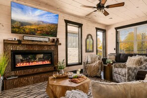 A cozy living room with a fireplace, comfortable seating, a television, and a view of the outdoors.