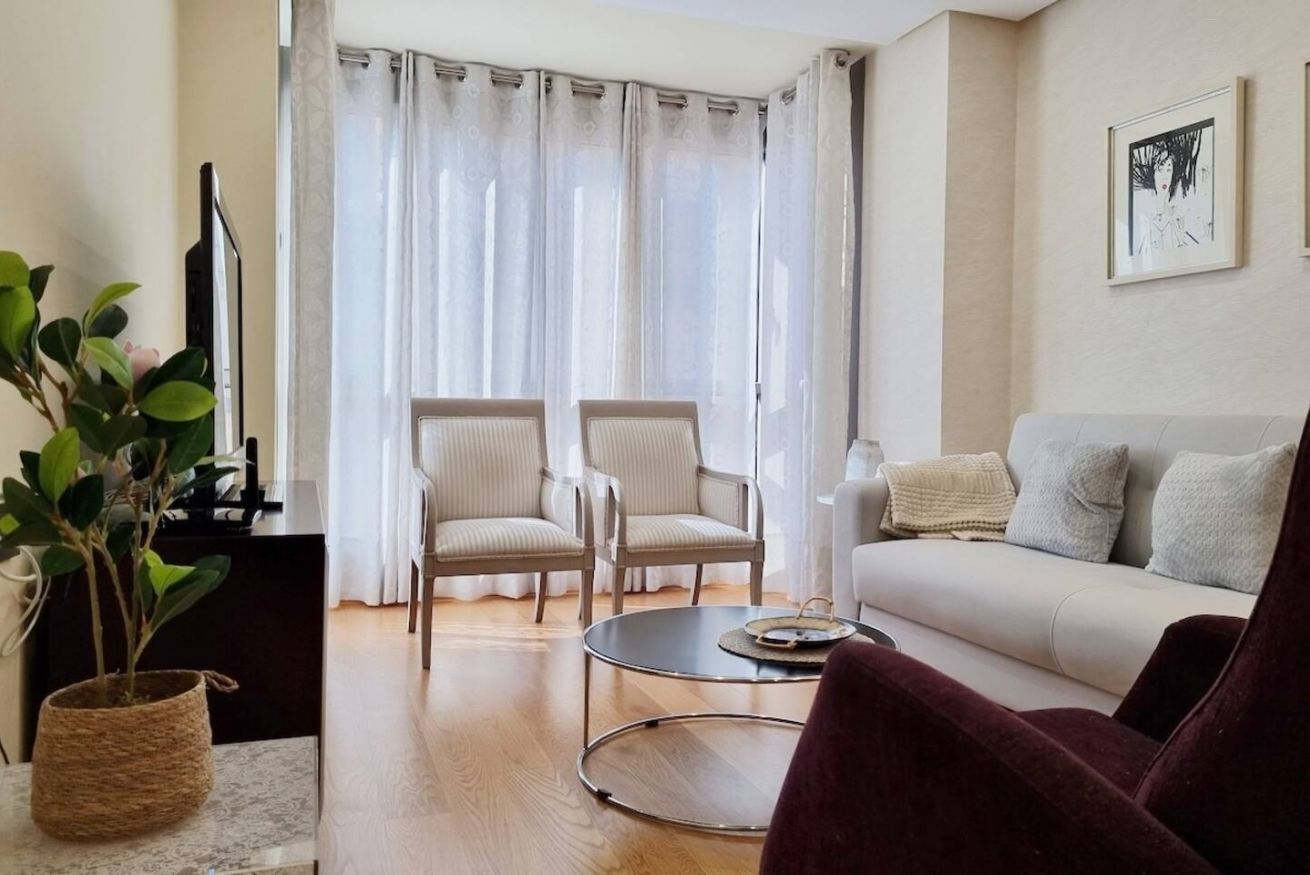 A living room with a sofa, two armchairs, a coffee table, a plant, and a painting on the wall.