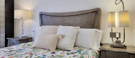 A neatly made bed with a floral bedspread, a bedside table with a lamp, and a nightstand with a lamp.