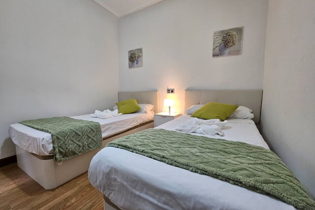 Een hotelkamer met twee eenpersoonsbedden, een nachtkastje met een lamp en twee kunstwerken aan de muur.