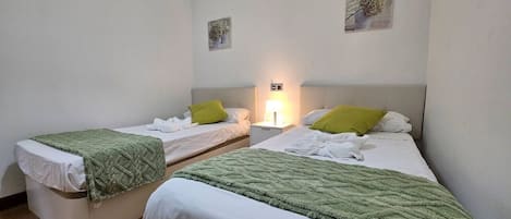 Habitación de hotel con dos camas individuales, una mesita de noche con lámpara y dos obras de arte colgadas en la pared.