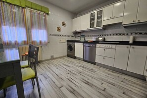 A kitchen with a washing machine, dishwasher, and a dining area with a table and chairs.