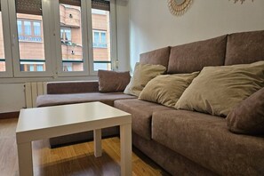 A living room with a brown sofa, a white table, and a view of a brick building through a window.