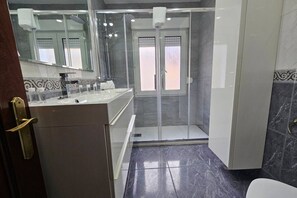 Un baño moderno con cabina de ducha de vidrio, tocador con espejo y suelo de mármol.