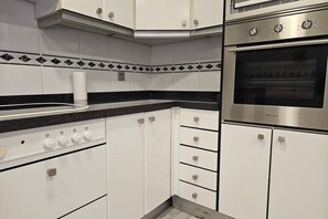 A kitchen with white cabinets, a stainless steel oven, a black countertop, and a paper towel dispenser.