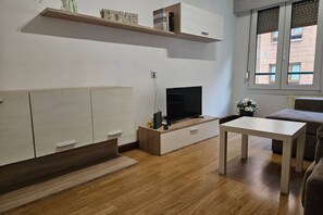 A modern living room with a TV, wooden flooring, a white table, and a sofa.