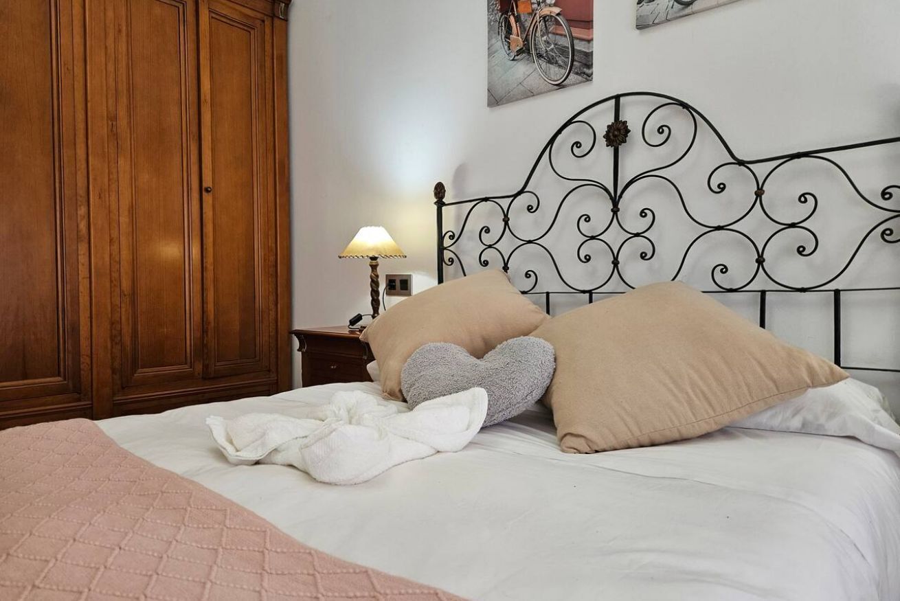 Un dormitorio con cama, armario de madera, cabecera de metal y una mesita de noche con lámpara.