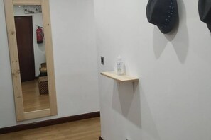 A hallway with a wooden floor, a mirror, a shelf with a bottle, and a fire extinguisher.