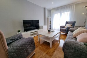 Uma sala de estar moderna com uma televisão de tela plana, uma mesa de centro branca e dois sofás.