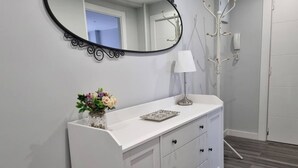 Une salle de bain avec un meuble-lavabo blanc, un miroir, un vase avec des fleurs et une lampe.