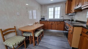 Une cuisine équipée d’une table à manger, de chaises, de meubles de rangement en bois, d’un four à micro-ondes et d’une fenêtre.
