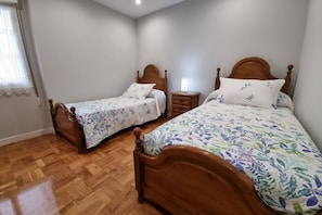 Un dormitorio con dos camas de madera, una mesita de noche y una ventana con cortina.