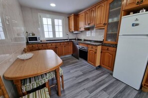 A kitchen with wooden cabinets, a white refrigerator, a microwave, a stove, and a dining table with chairs.