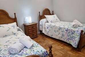 Una camera da letto con due letti di legno, ognuno con una coperta a fiori e un cuscino bianco. Tra i letti, un comodino in legno con una lampada.