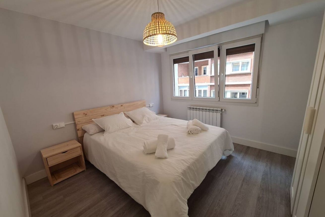 Un dormitorio con cabecera de madera, una mesita de noche y un radiador, además de una ventana con persianas.