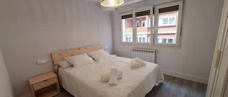 Un dormitorio con cabecera de madera, una mesita de noche y un radiador, además de una ventana con persianas.
