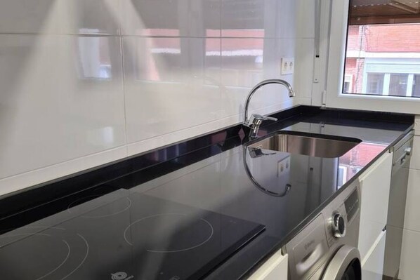 A modern kitchen with a black countertop, stainless steel sink, and a built-in washing machine.