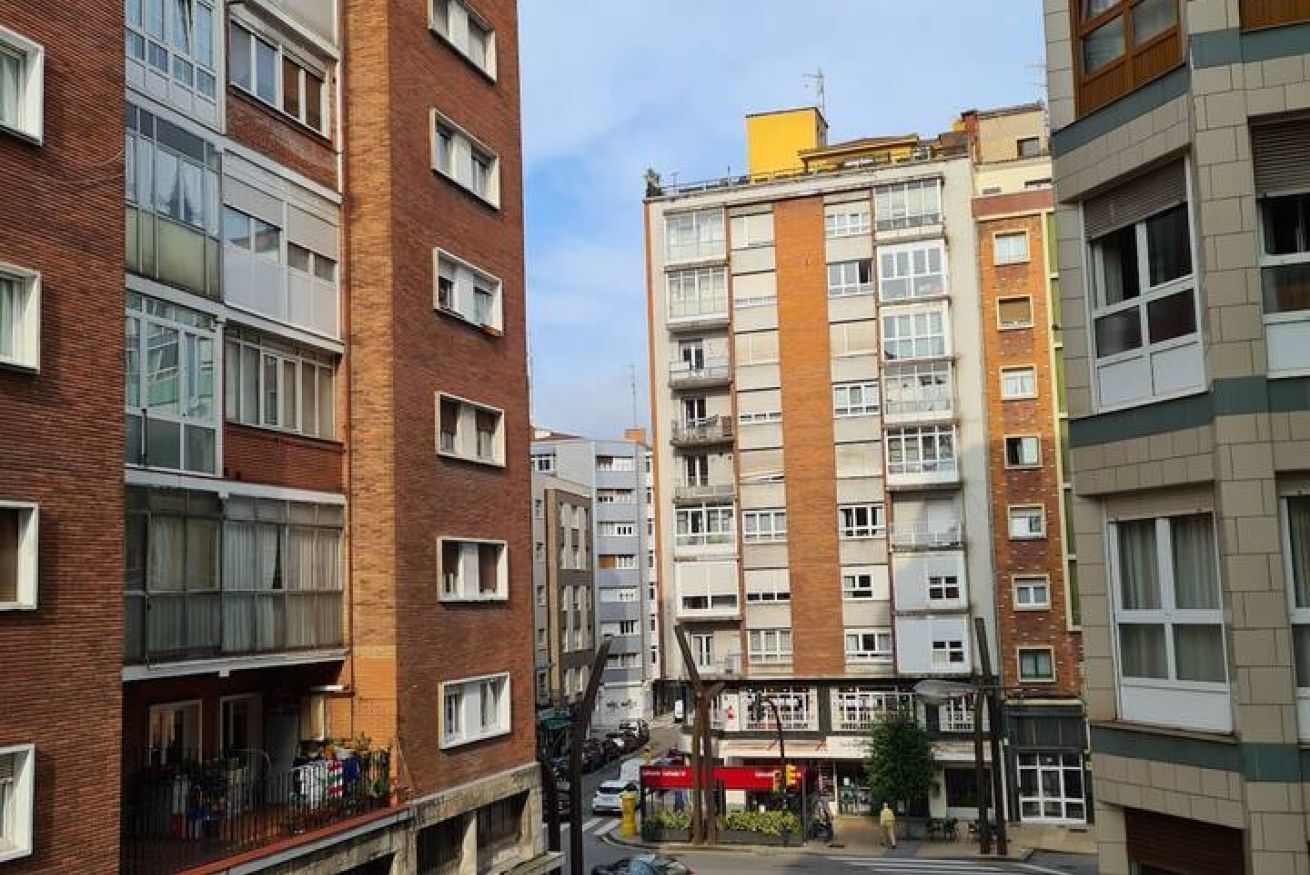 Un edificio residencial de varios pisos, con balcones, una planta baja con tiendas y un cielo despejado.