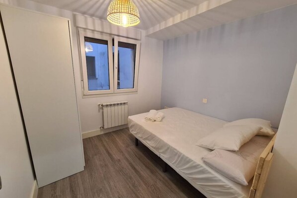 A bedroom with a bed, a window, a radiator, and a wardrobe.