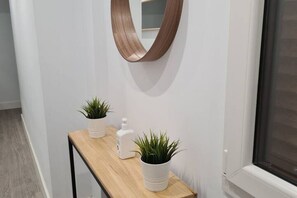 A hallway with a wooden console table, two potted plants, a white bottle, and a wooden-framed mirror on the wall.